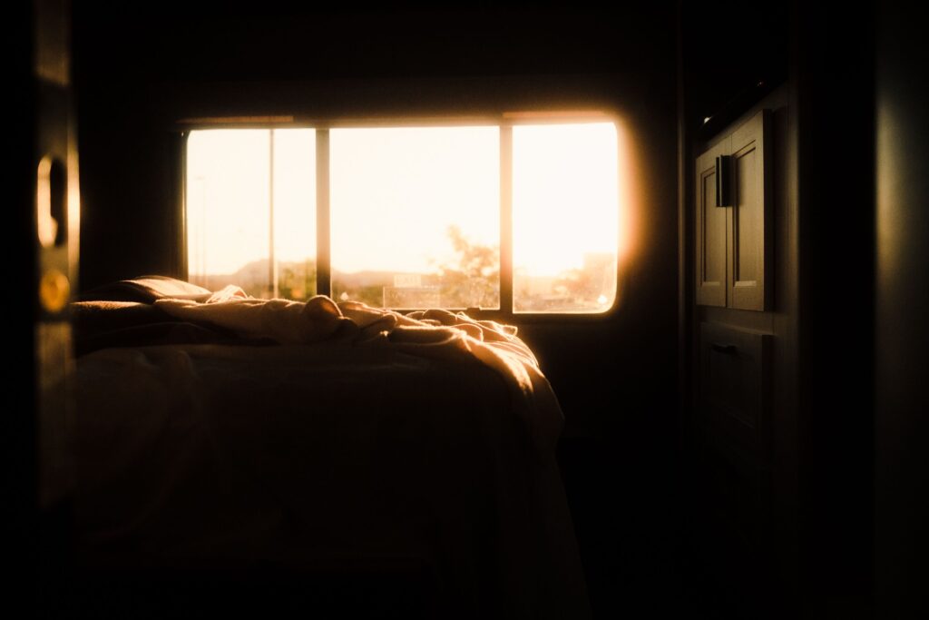 A beautiful wide shot of a tranquil bedroom interior bathed in warm sunrise light streaming through the window. The serene and quiet atmosphere beautifully symbolizes the return of proportion, the boundary between rest and worry, and the bodily feeling of greeting the new day without the exhaustion of borrowed tomorrows, highlighting the core themes of the blog "The Day We Live Twice" by Dhrruv Tokas.